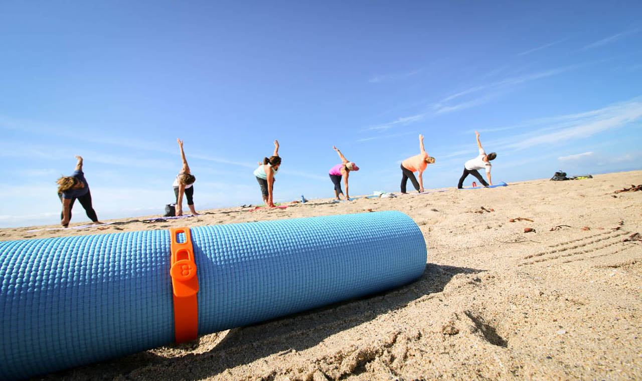 A Packband secures a rolled yoga mat in front of beach yoga